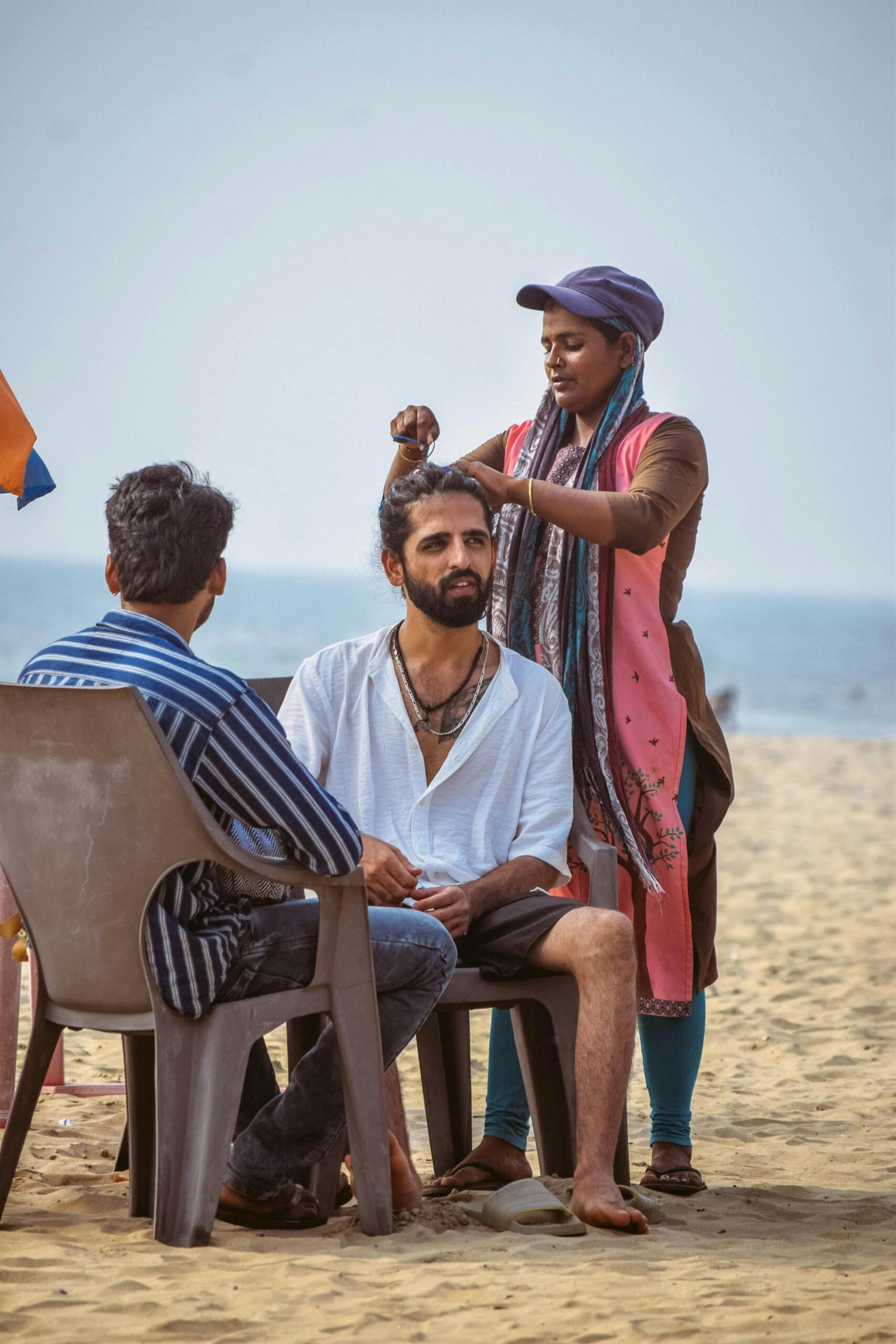 Beachside hair braiding in Arambol, Goa, with people enjoying the relaxed atmosphere.