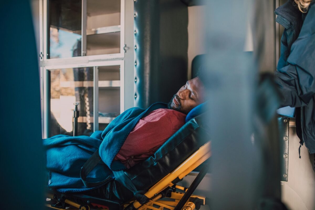 A serene depiction of an African American man resting on a stretcher in a medical vehicle, wrapped in a blue blanket.